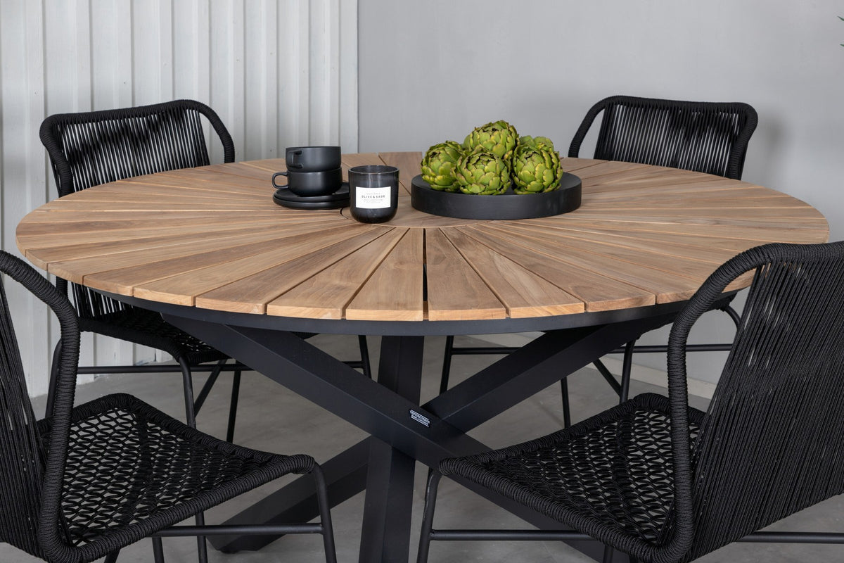 Vier schwarze Esszimmerstühle mit Aluminiumgestell und Polyesterbezug neben rundem Teak-Esstisch mit Stahlbeinen, Durchmesser 140 cm.