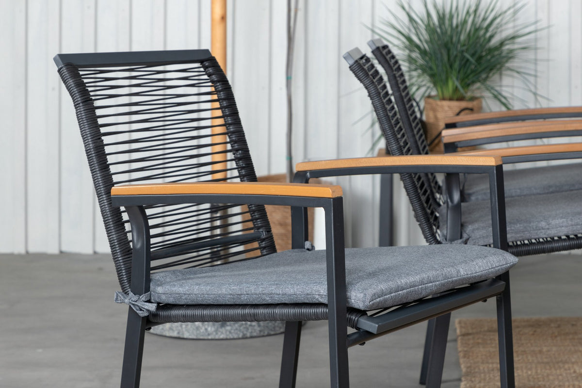 Foto eines schwarzen 2er-Stuhlsets mit Aluminiumgestell und Polyesterbezug neben einem rechteckigen Teak-Esstisch in Natur mit Stahlbeinen.