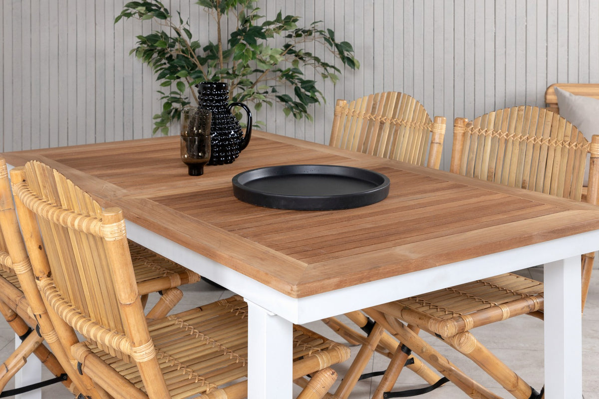Foto zeigt einen Cafe Stuhl mit Rattan-Beinen und Stoffbezug in Natur sowie einen rechteckigen Teakholz-Esstisch mit weissem Aluminiumgestell.