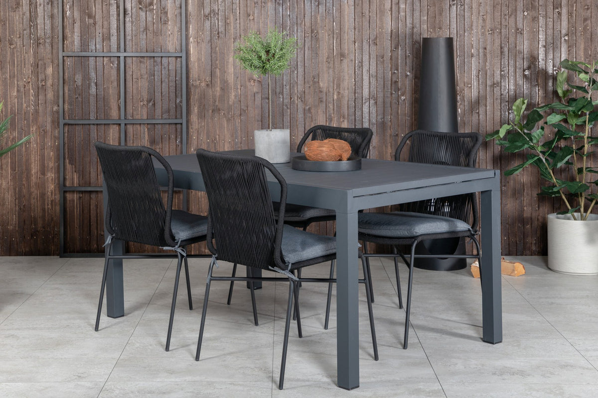 Vier schwarze Esszimmerstühle mit Polyesterbezug und pulverbeschichtetem Aluminiumgestell neben einem rechteckigen Esstisch aus schwarzem Aluminium.