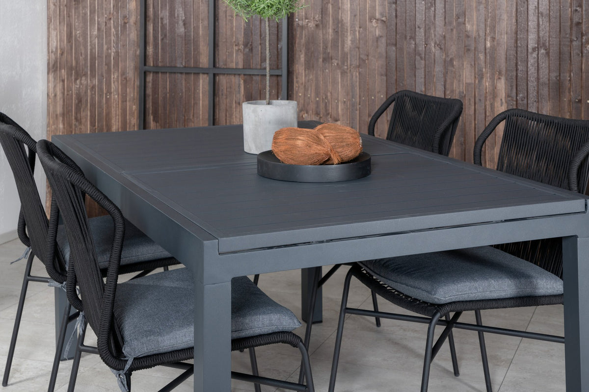 Vier schwarze Esszimmerstühle mit Polyesterbezug und pulverbeschichtetem Aluminiumgestell neben einem rechteckigen Esstisch aus schwarzem Aluminium.