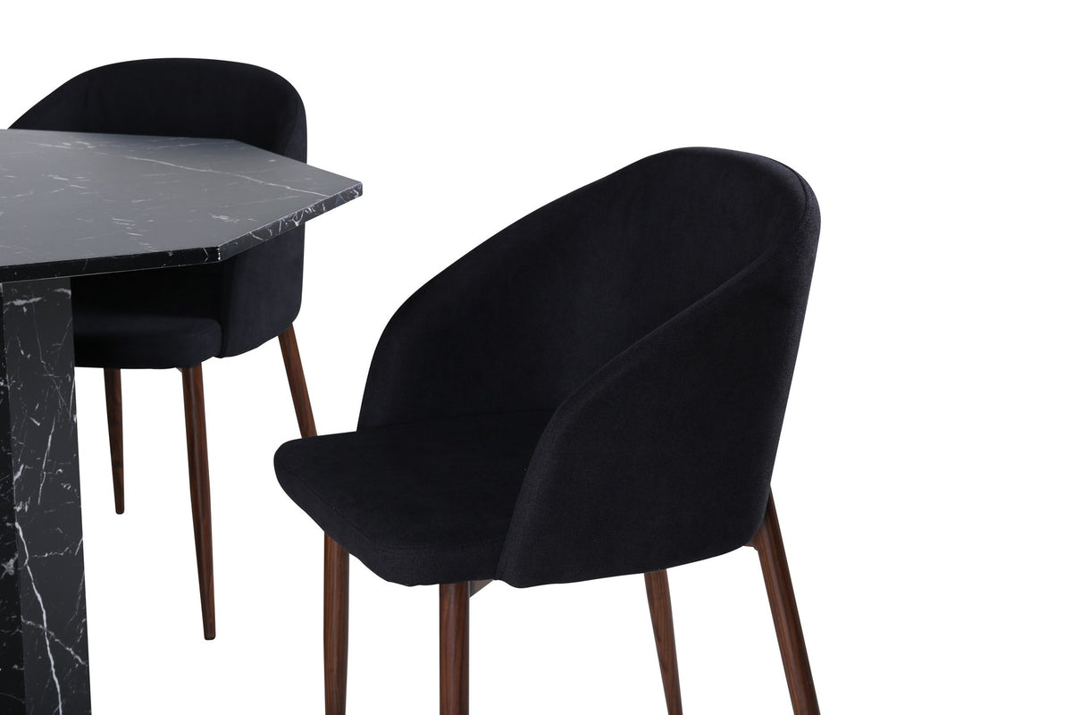 Zwei schwarze Esszimmerstühle mit Nussbaum-Beinen und Polyester-Sitzfläche neben rundem Esstisch Ø110cm mit schwarzer MDF-Platte und Stahlbeinen.