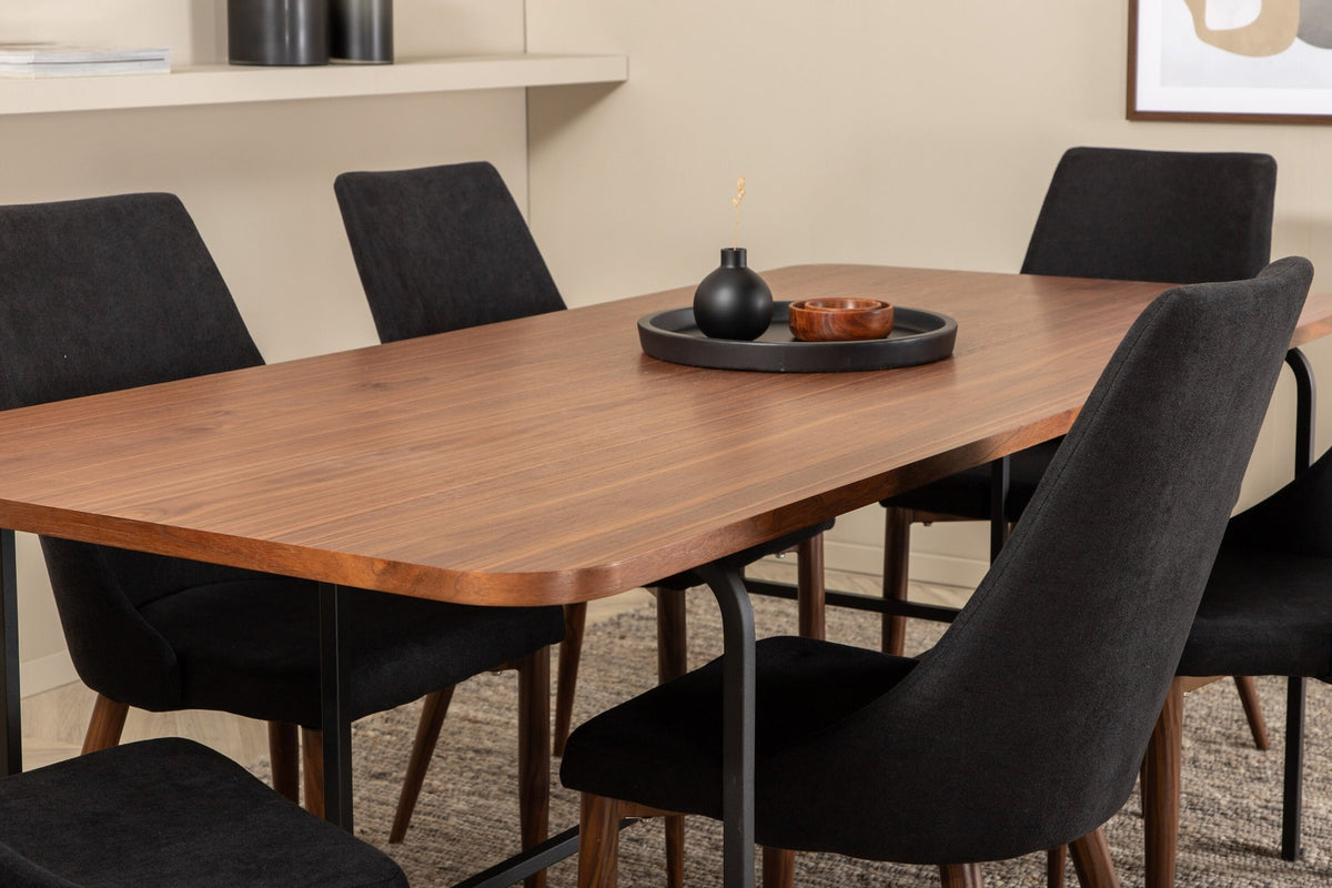 Rechteckiger Esstisch mit MDF-Tischplatte in Nussbaumfurnier und schwarzem Stahlgestell, kombiniert mit zwei schwarzen Polyester-Stühlen.