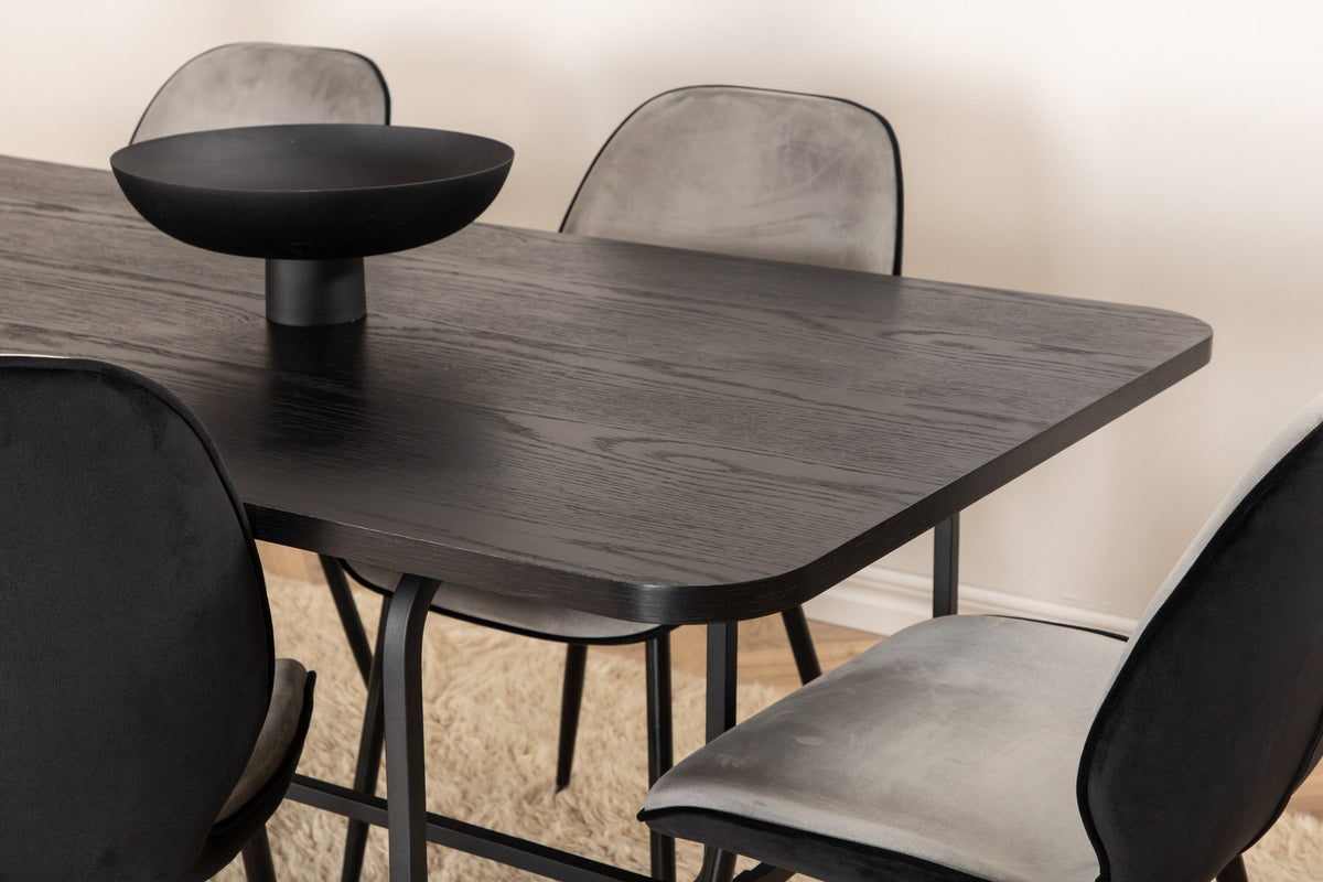 Zwei graue Esszimmerstühle mit Samtbezug und Eisenbeinen neben einem rechteckigen schwarzen Esstisch aus MDF mit Furnier und Metallgestell.