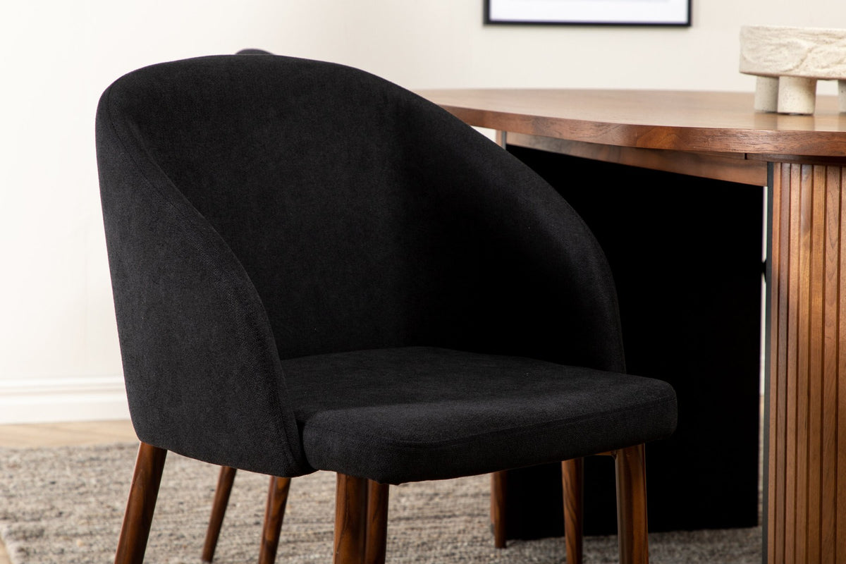 Ovaler Esstisch mit Nussbaum-MDF-Furnierplatte und Stahlgestell, daneben zwei schwarze Polsterstühle mit Metallbeinen im Esszimmer.