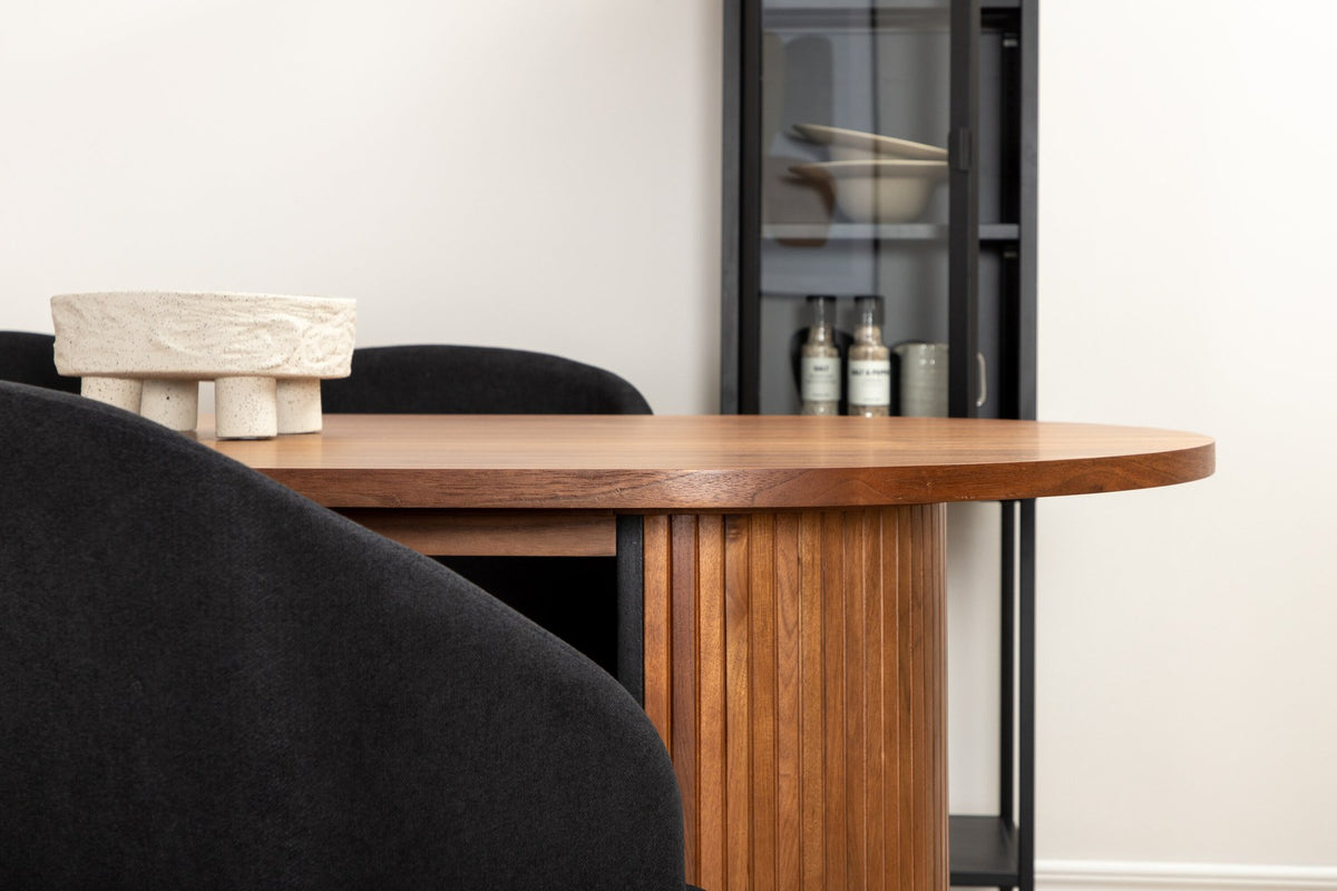 Ovaler Esstisch mit Nussbaum-MDF-Furnierplatte und Stahlgestell, daneben zwei schwarze Polsterstühle mit Metallbeinen im Esszimmer.