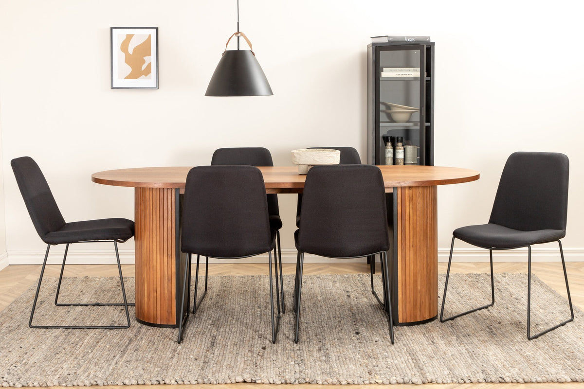 Ovaler Esstisch mit Nussbaum-Furnier und MDF-Platte, kombiniert mit zwei schwarzen Esszimmerstühlen mit Polyesterbezug und schmalen Stahlbeinen.