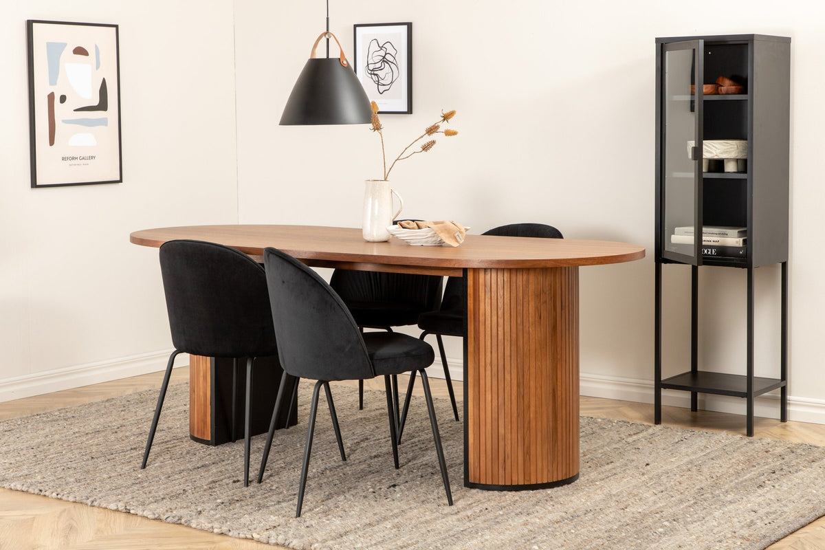 Zwei schwarz gepolsterte Esszimmerstühle mit Samtbezug und Metallgestell neben ovalem Esstisch mit Nussbaum-Furnierplatte und Stahlgestell.
