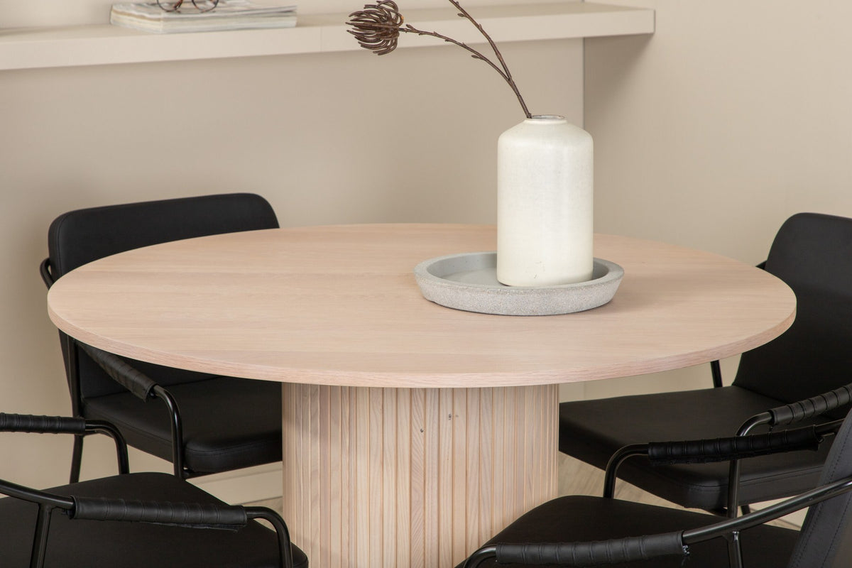 Rundes Esszimmerset aus MDF: Tischplatte Ø110 cm in Whitewash mit gerippten Beinen, dazu zwei schwarze Stühle mit Eisenbeinen.