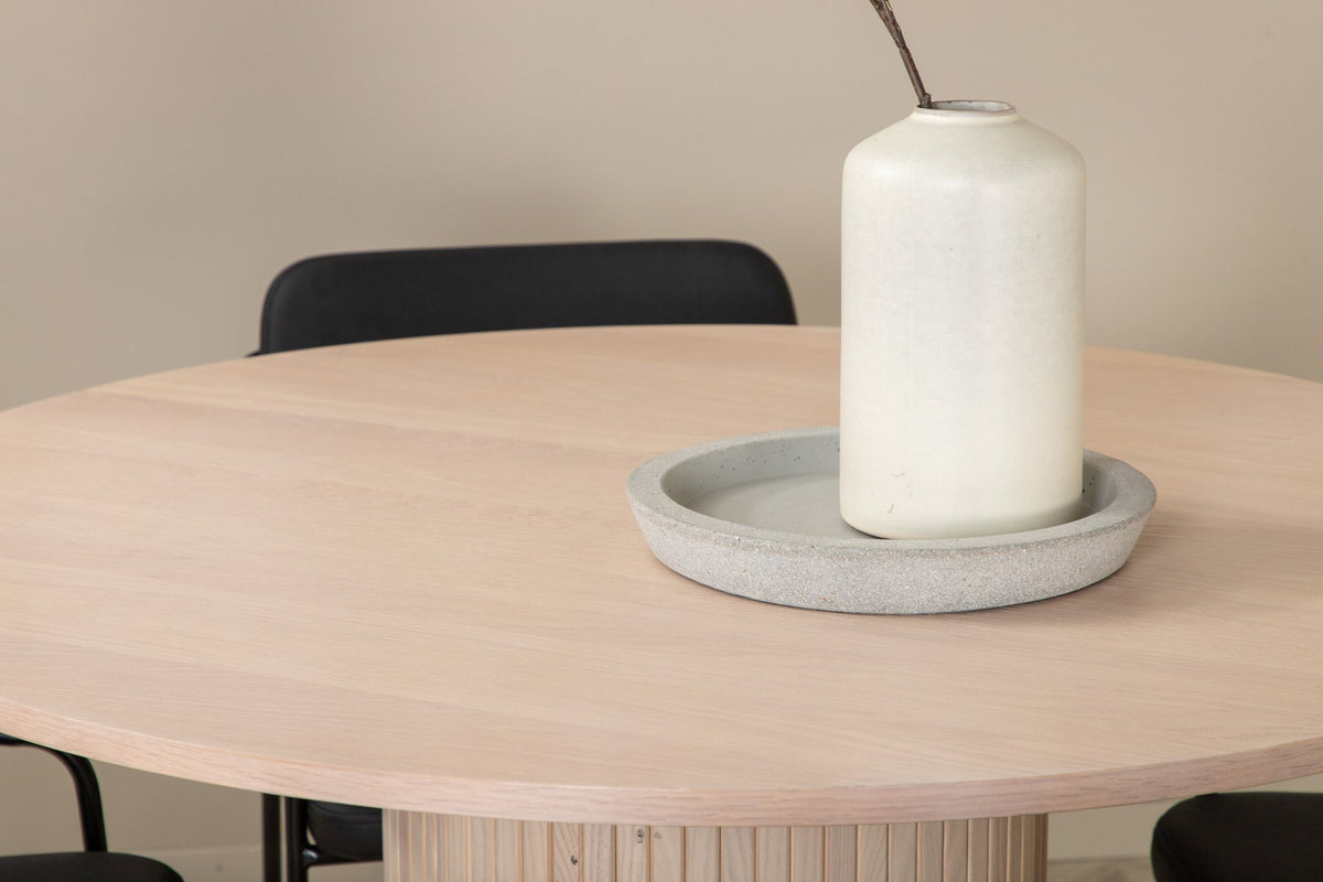 Rundes Esszimmerset aus MDF: Tischplatte Ø110 cm in Whitewash mit gerippten Beinen, dazu zwei schwarze Stühle mit Eisenbeinen.