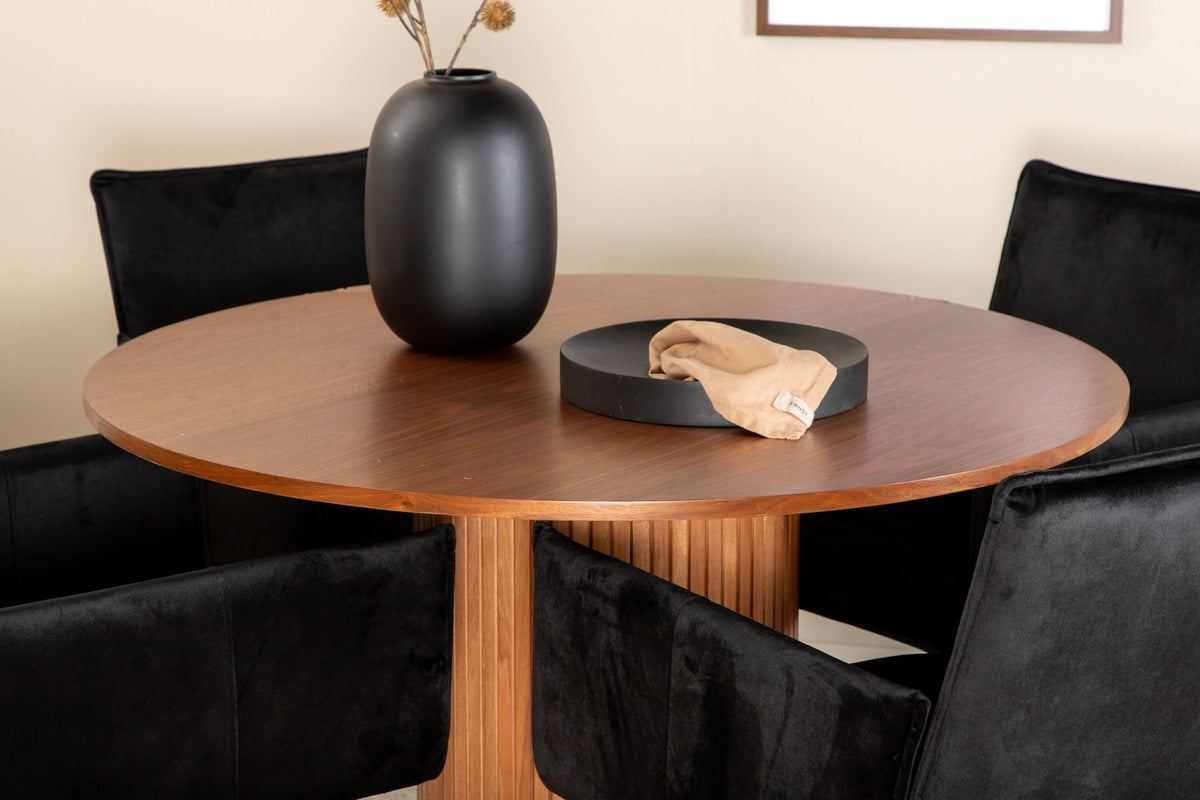 Rundes Esszimmerset mit Nussbaum-Tischplatte Ø110cm aus MDF und vier schwarzen Stühlen mit Samtsitz und Beinen aus Eisen.