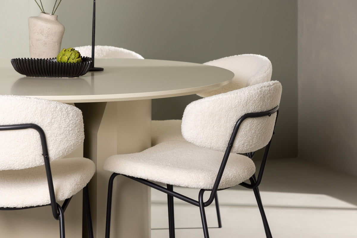 Zwei weisse Esszimmerstühle mit Bouclé-Bezug und schwarzem Stahlgestell neben rundem MDF-Esstisch mit beiger Tischplatte, Durchmesser 140 cm.