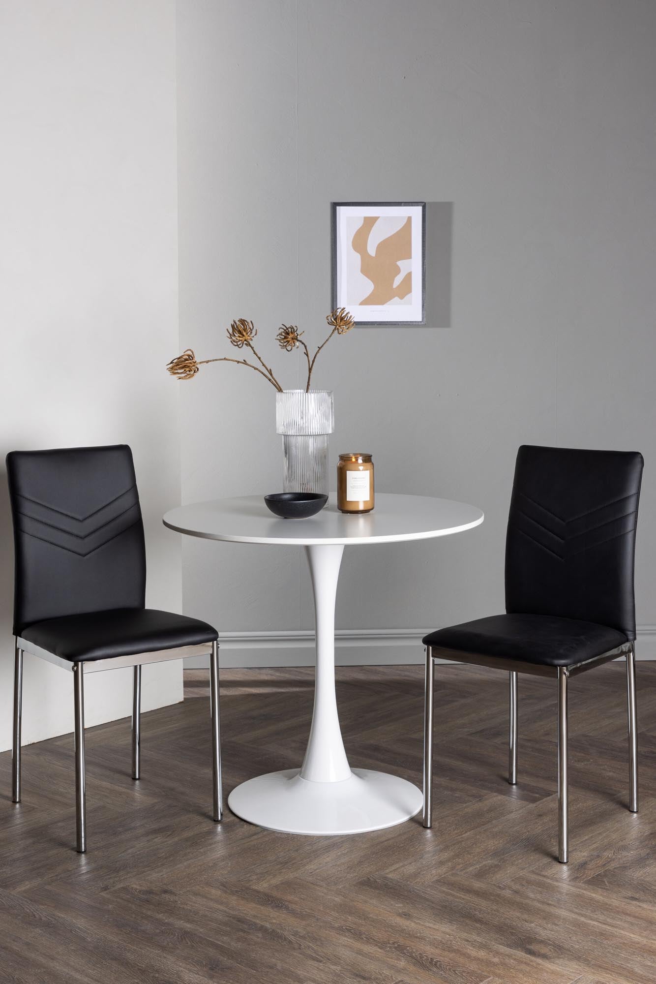 Elegantes Esszimmerset: Weisser MDF-Tisch mit Stahlfuss, schwarze Kunstlederstühle, ideal für kleine Räume.