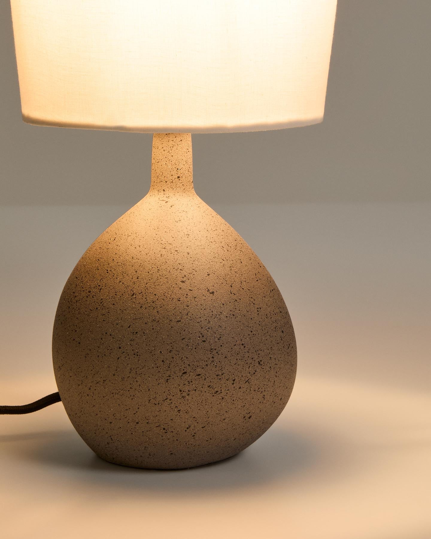 Kleine Tischlampe Viona in strukturierter Steinoptik mit einem Lampenschirm aus Baumwolle in Hellgrau präsentiert im Onlineshop von KAQTU Design AG. Tischleuchte ist von Kave Home