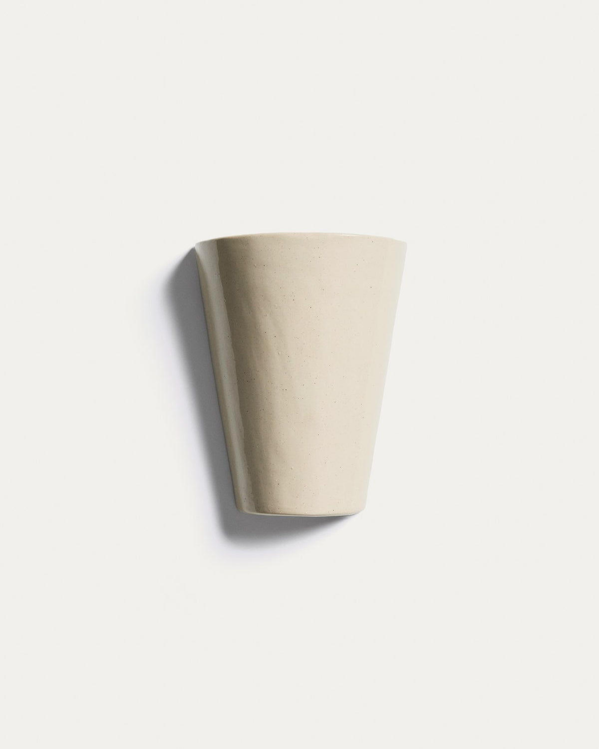 Beigefarbene Wandleuchte Ceren aus Keramik mit schlichter, runder Form, montiert an einer hellen Wand, Grösse 12 x 6 x 14 cm.