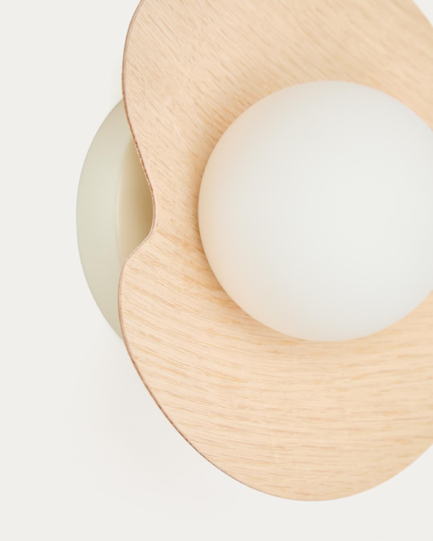 Die Wandleuchte Wilara von Kave Home kombiniert stilvolles Eichenfurnier mit einer eleganten weißen Rauchglaskugel und sorgt für warmes, diffuses Licht.