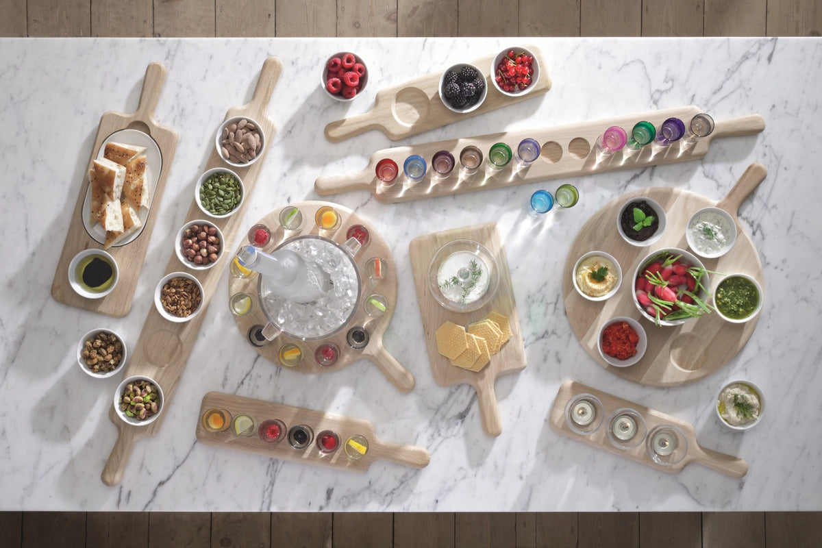 Paddle Wodka Set von LSA: sechs mehrfarbige Schnapsgläser aus Glas in Ombre-Optik auf einem länglichen Unterteil aus Eichenholz mit Griffen an beiden Enden.