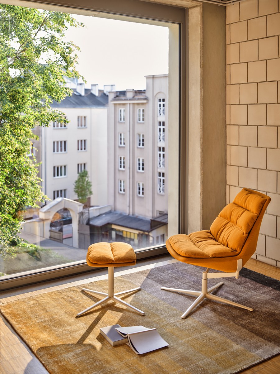 Ziegelroter Loungesessel mit gepolstertem Sitz, drapiertem Kissen und Aluminium-Drehfuss auf vier Sternbeinen, Frontalansicht.