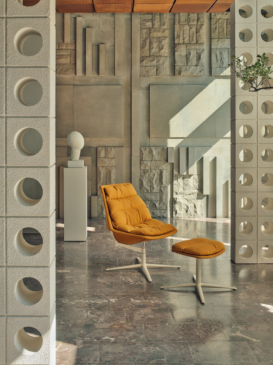 Ziegelroter Loungesessel mit gepolstertem Sitz, drapiertem Kissen und Aluminium-Drehfuss auf vier Sternbeinen, Frontalansicht.