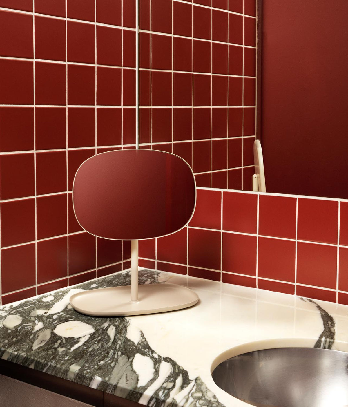 Tischspiegel Flip von Normann Copenhagen mit rundem Glasspiegel und Fuss aus beschichtetem Stahl in organischer Form, Farbe Schwarz.