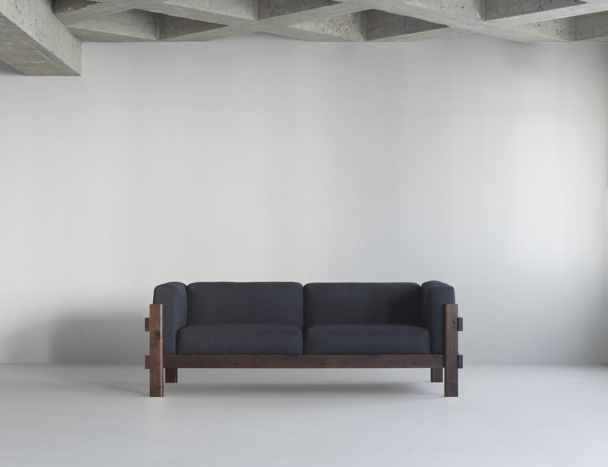 Kube 3er Sofa in Anthrazit von Normann Copenhagen mit sichtbarem Kiefernholz-Rahmen und lose aufliegenden Polsterkissen.