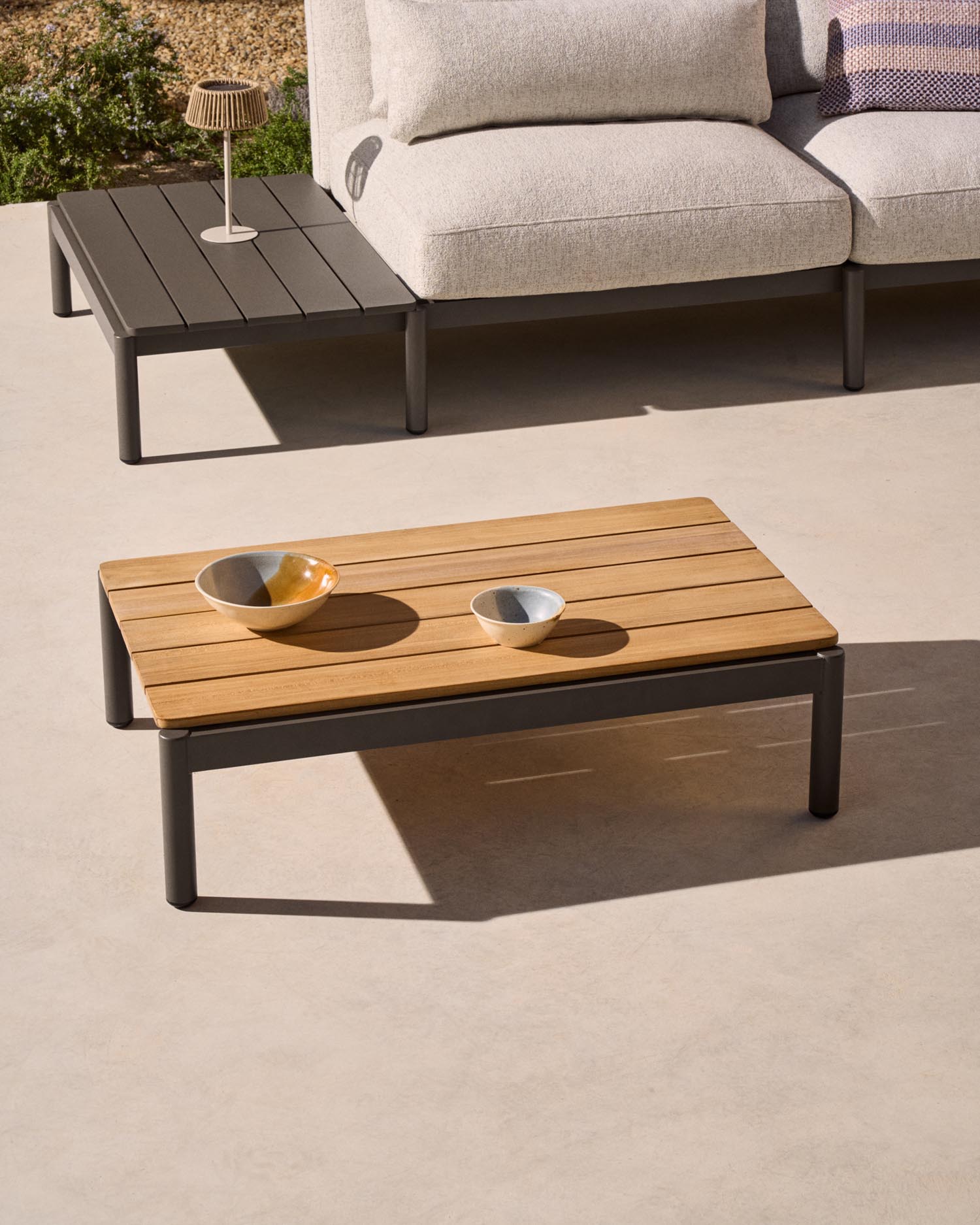 Entdecken Sie den stilvollen Couchtisch Sorells aus grauem Aluminium und Teakholz – ideal für Ihre Outdoor-Oase. Robust, elegant und vielseitig!