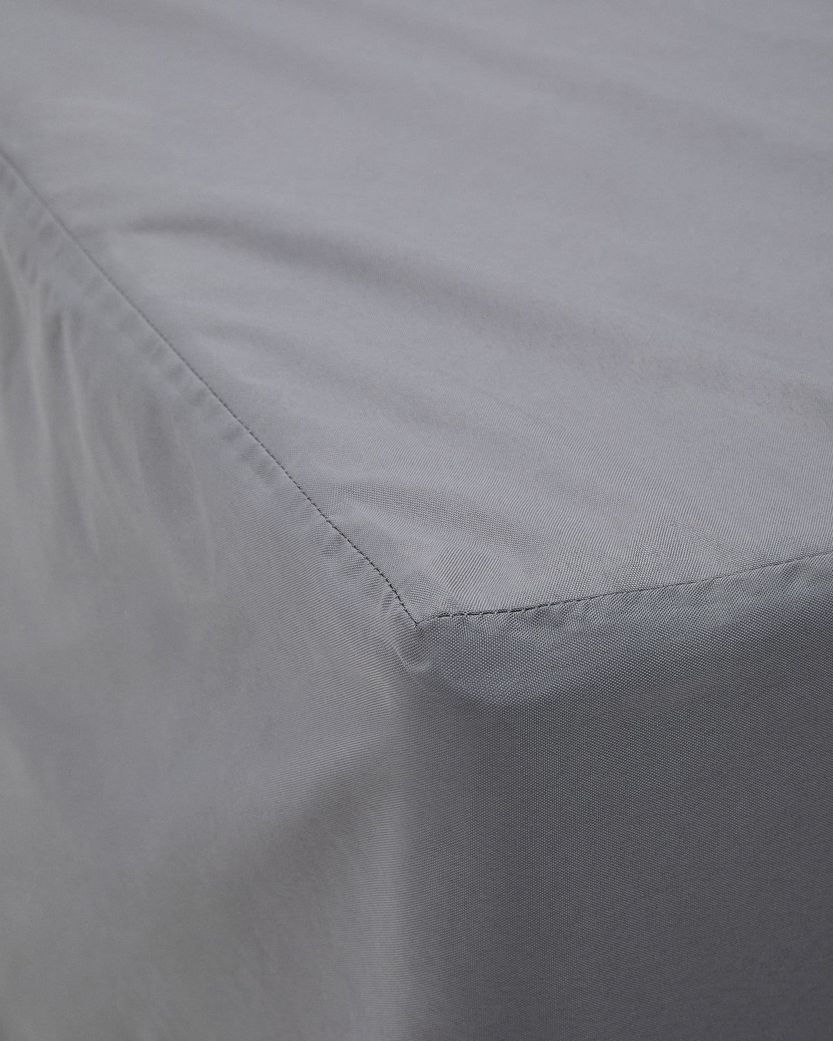 Graue Schutzhülle aus Polyester für Outdoor-Möbel, mit verschweissten Nähten und Belüftungsfenster, auf einer Sonnenliege drapiert.