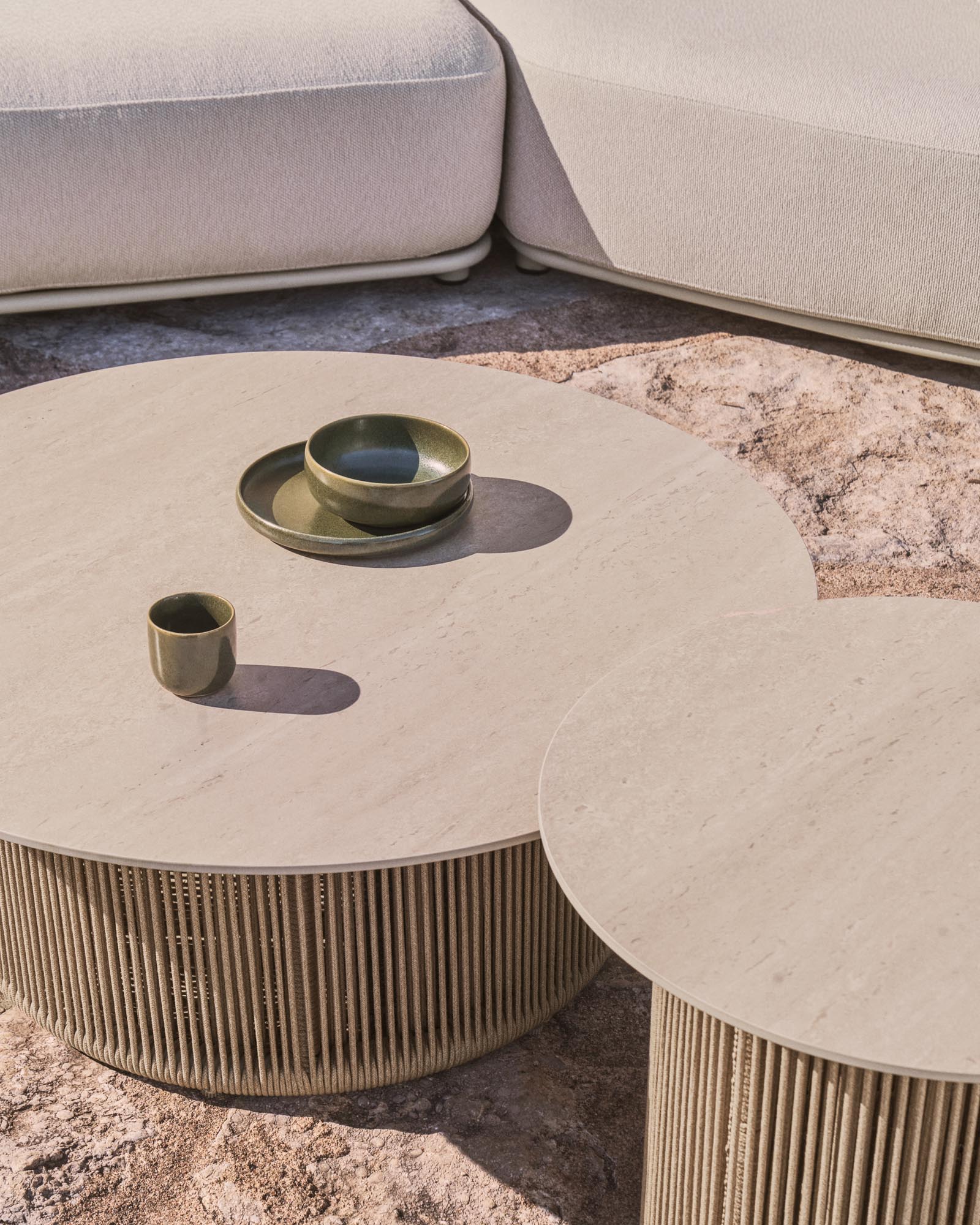 Eleganter Outdoor-Couchtisch Orosei mit Ø 90 cm, gefertigt aus Sinterstein und Aluminium, umgeben von beigem Seil für stilvolle Entspannung.