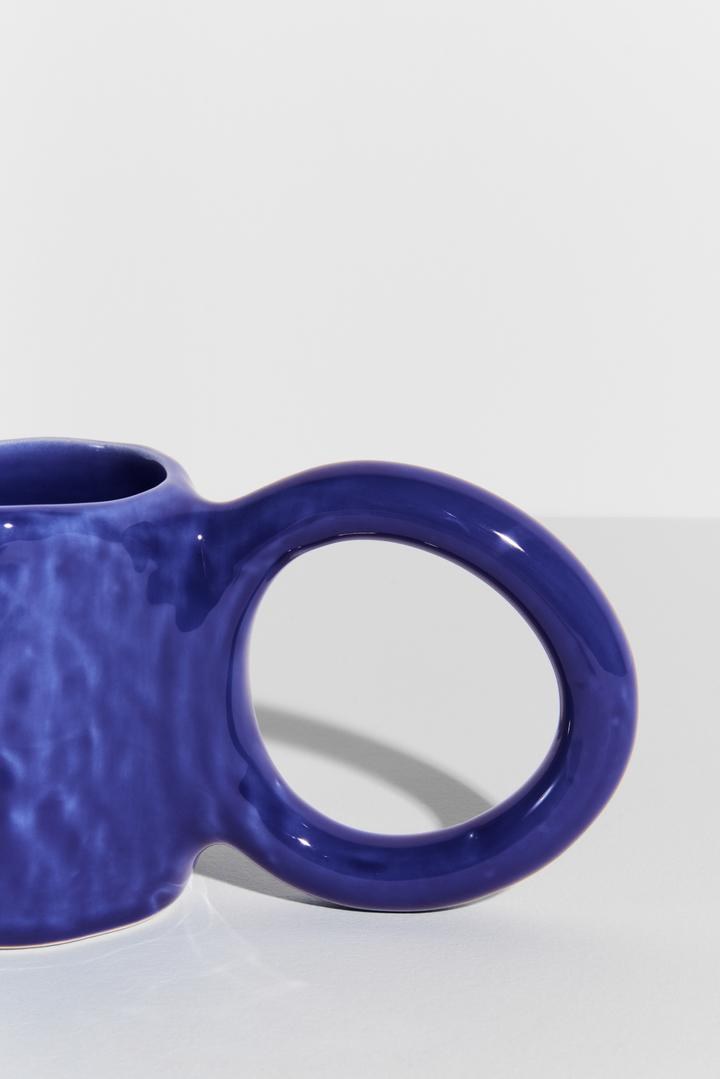 Keramiktasse Donut in Pistazie mit glasierter Oberfläche und donutförmigem Henkel, mittlere Grösse, handwerklicher Look, auf hellem Hintergrund.