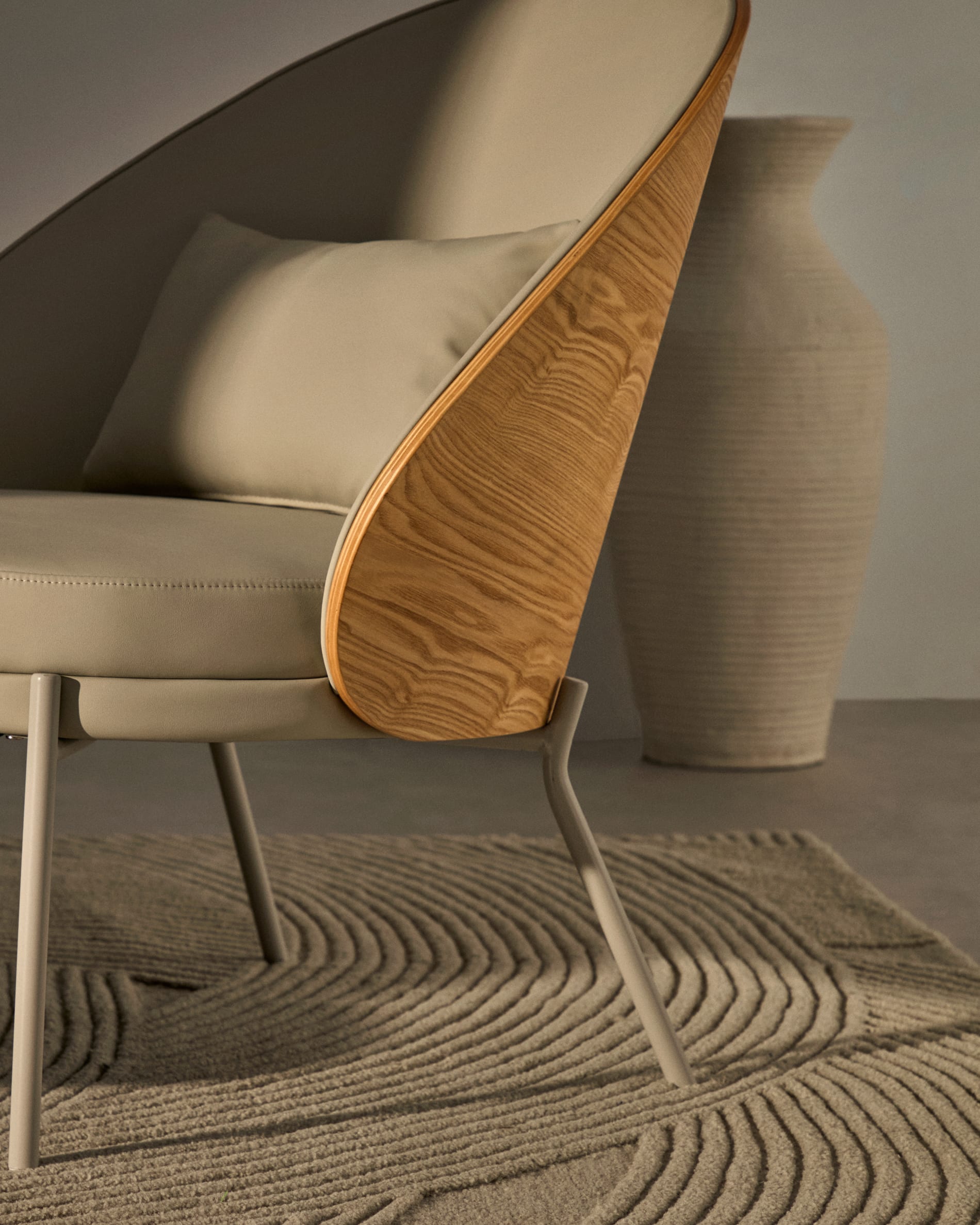 Moderner Eamy Sessel: Beigefarbenes Kunstleder, edles Eschenfurnier in Nussbaum-Finish, stabiler Metallrahmen. Perfekt für stilvolle Wohnräume.