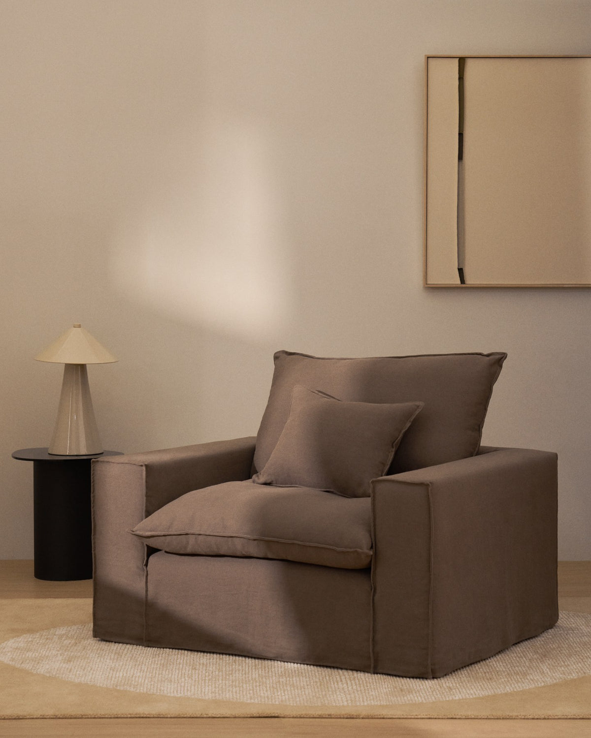 Sessel Anarela mit abnehmbarem Leinenbezug in Taupe, schwarzen Kunststoffbeinen und gepolsterter Sitzfläche, Frontalansicht.