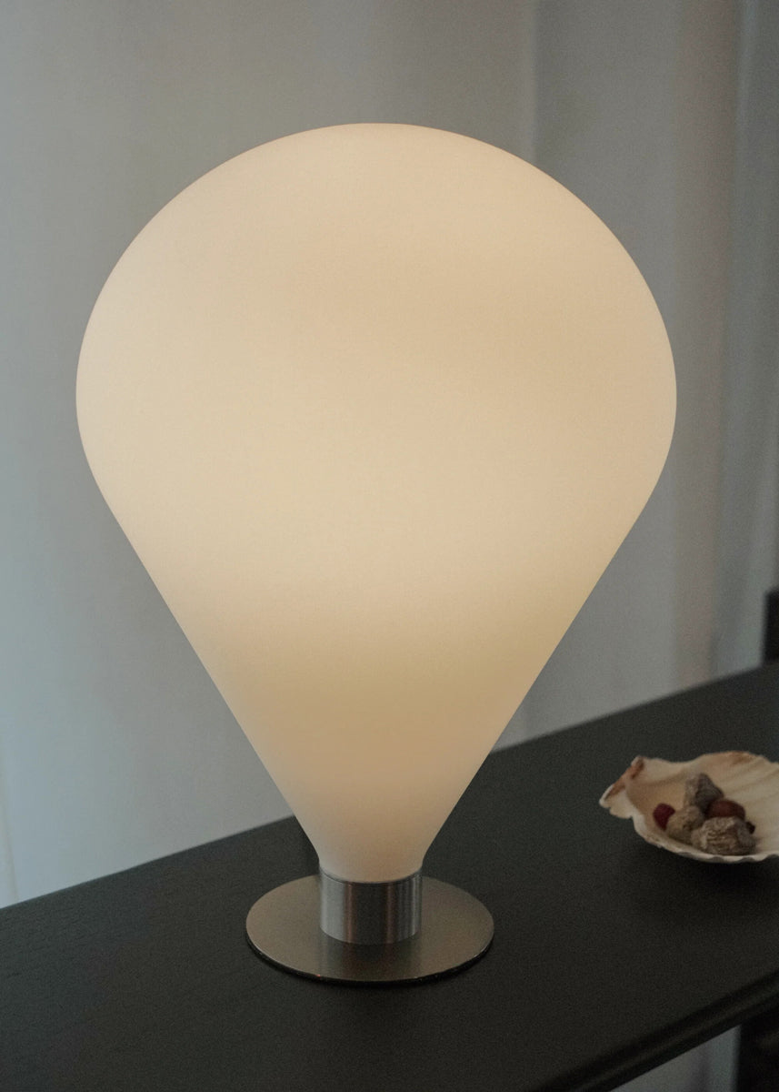 Elegante Ely ELY01 Tischleuchte von Tamo, harmonisch auf einem hellen Tisch inszeniert, vereint modernes Metall und Glas für ein warmes Ambiente.
