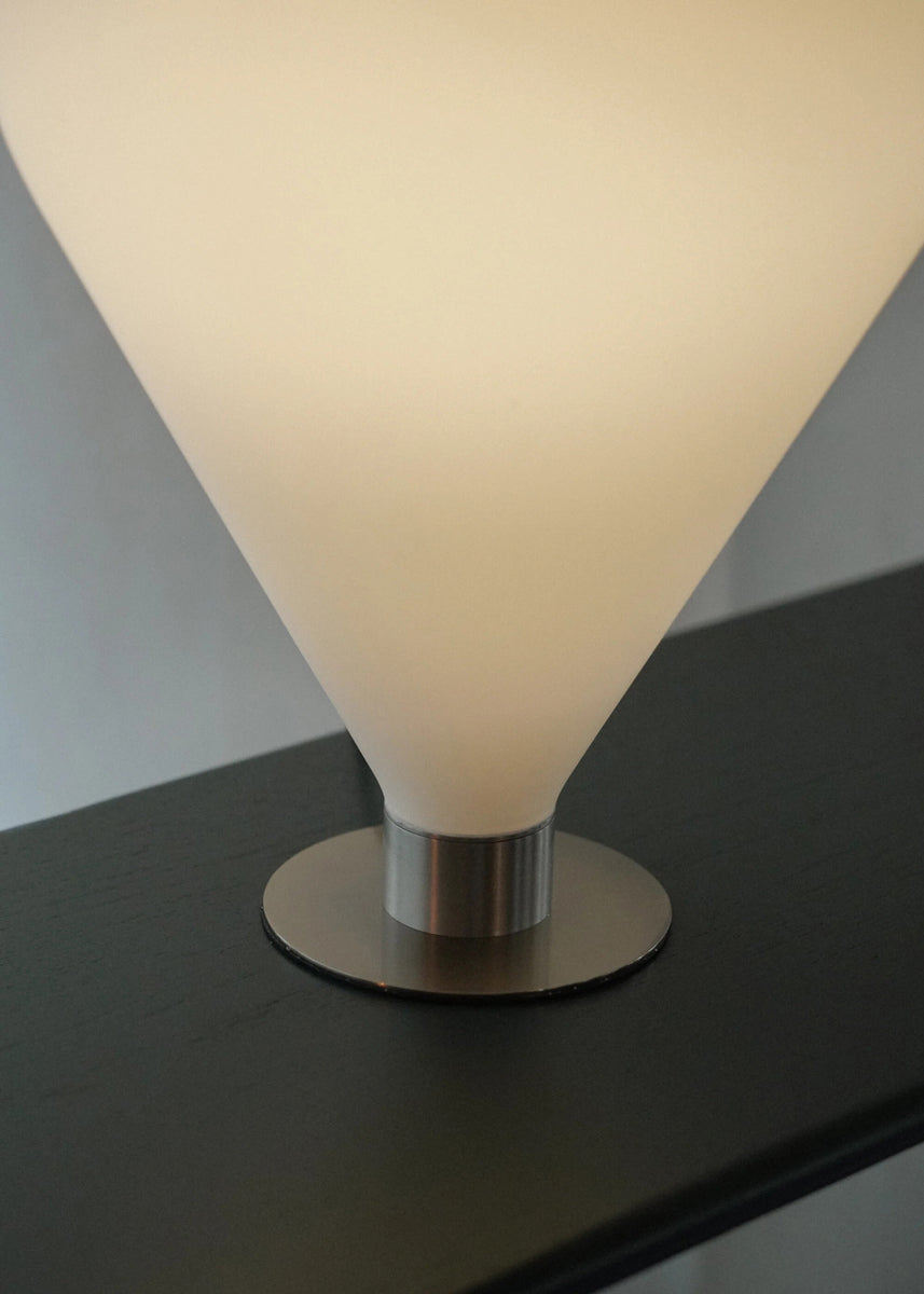 Stimmungsvolle Ely ELY01 Tischleuchte von Tamo, stilvoll auf einem hellen Tisch platziert, kombiniert edles Metall und Glas für eine einladende Atmosphäre.