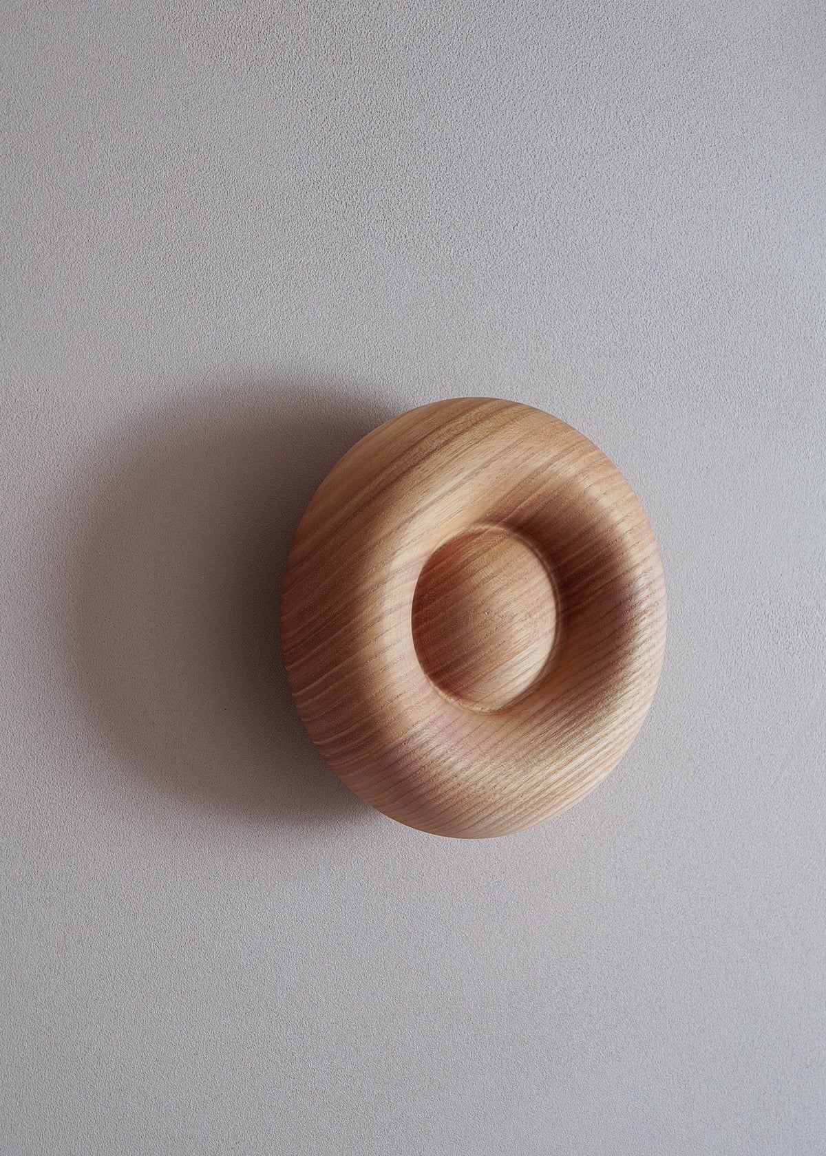 Blop Kleiderhaken von Tamo aus geöltem Massivholz in Esche, runde organische Form, an weisser Wand montiert, natürliche Maserung sichtbar.