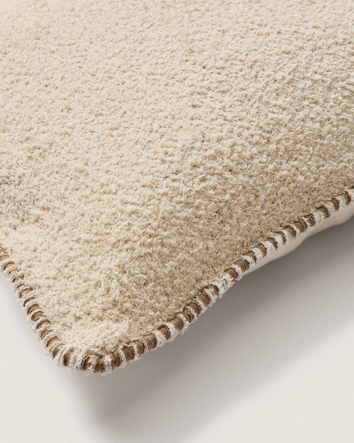 Beige quadratischer Kissenbezug aus Baumwoll-Bouclé-Gewebe mit brauner Kontrastpaspel am Rand, Grösse 50 x 50 cm, Nahaufnahme der Textur.
