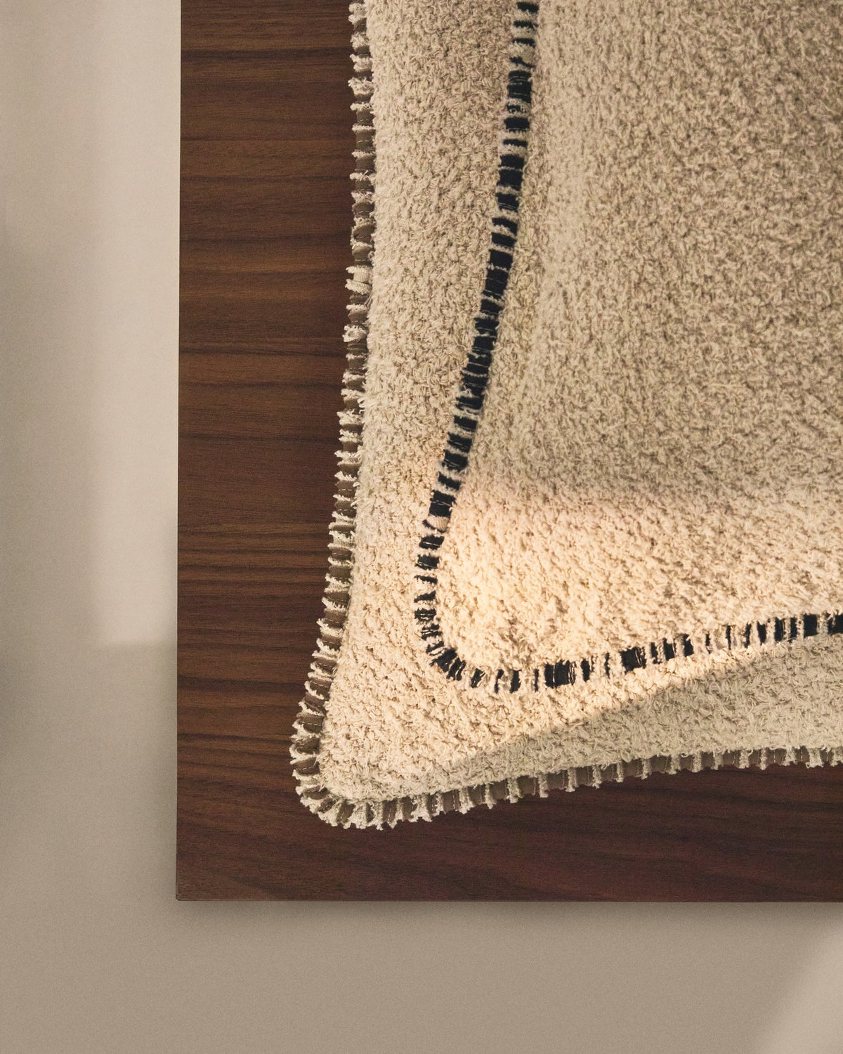 Beige quadratischer Kissenbezug aus Baumwoll-Bouclé-Gewebe mit brauner Kontrastpaspel am Rand, Grösse 50 x 50 cm, Nahaufnahme der Textur.