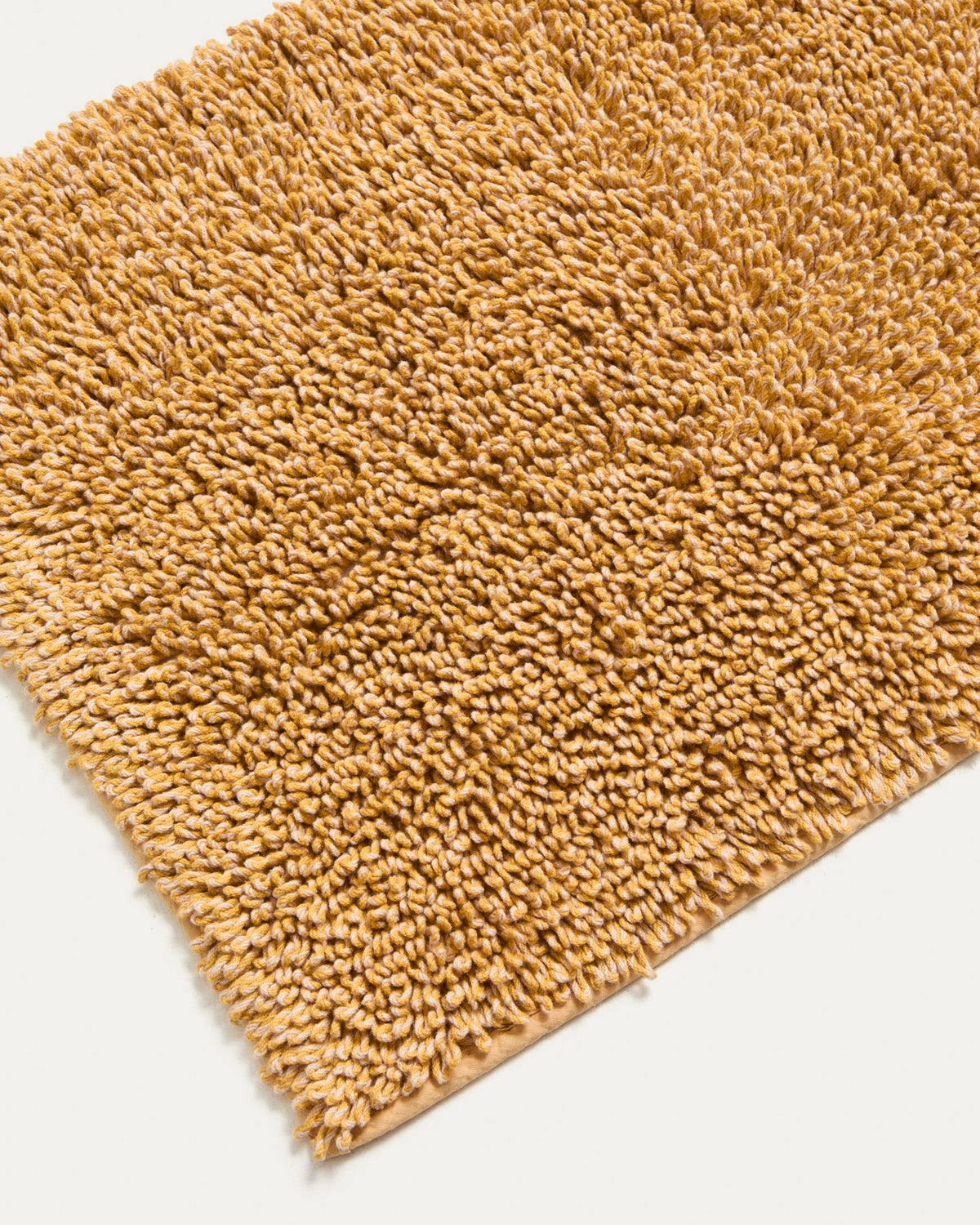 Senfgelbe Badezimmermatte Aroia von Kave Home mit Bouclé-Melange-Struktur in rechteckiger Form, Grösse 50 x 70 cm, auf Boden liegend.