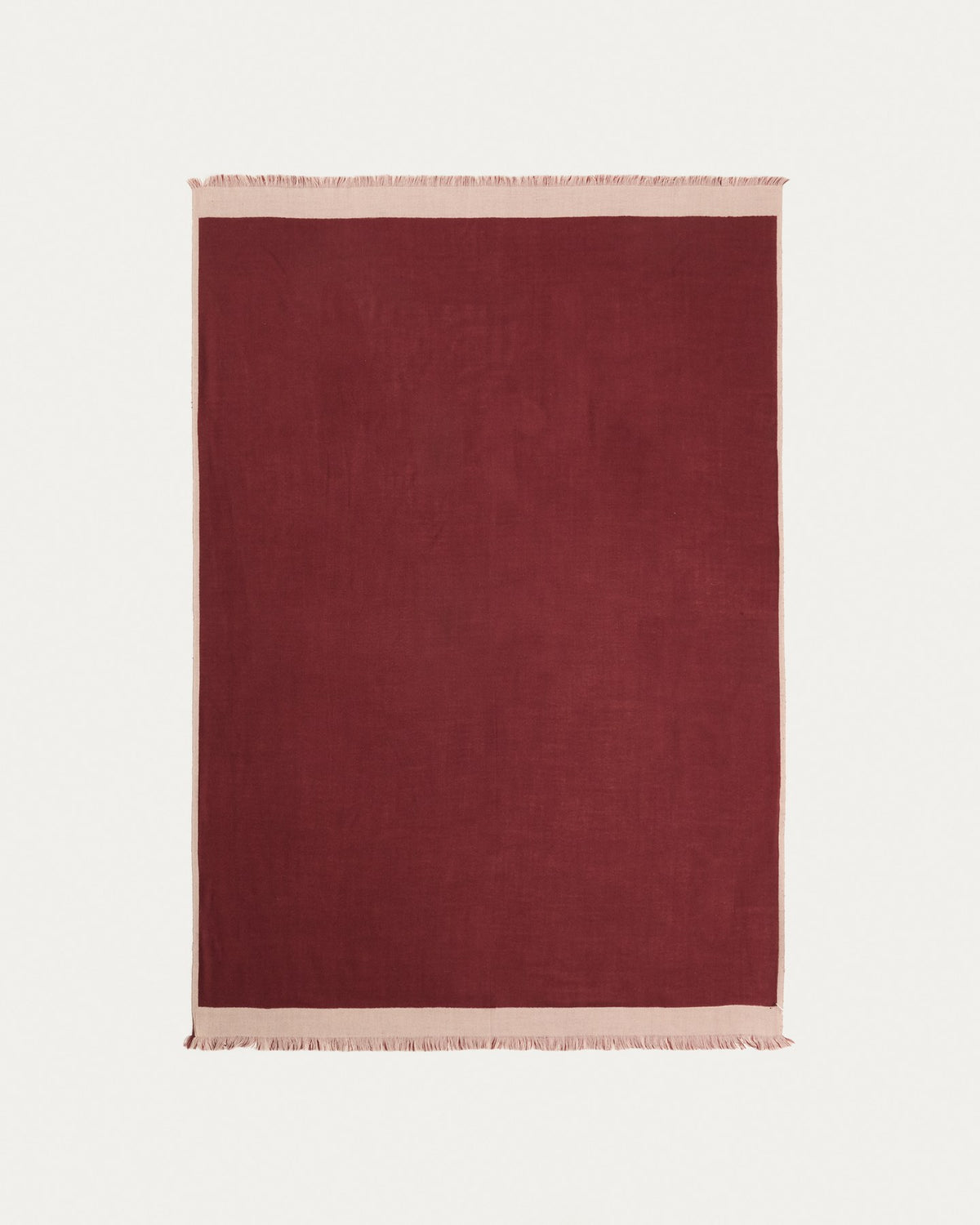 Wendbare Wolldecke aus 100% Wolle in Granatrot und Beige mit Fransen an den Rändern, gefaltet auf einem Sofa liegend.