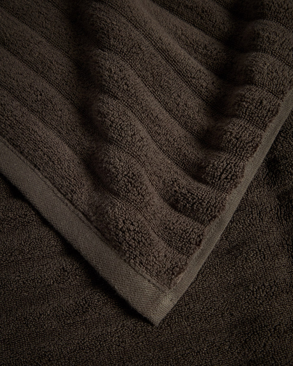 Dunkelbraunes Handtuch aus 100% Baumwolle mit welliger Struktur, rechteckige Form, Masse 50 x 90 cm, liegend fotografiert.