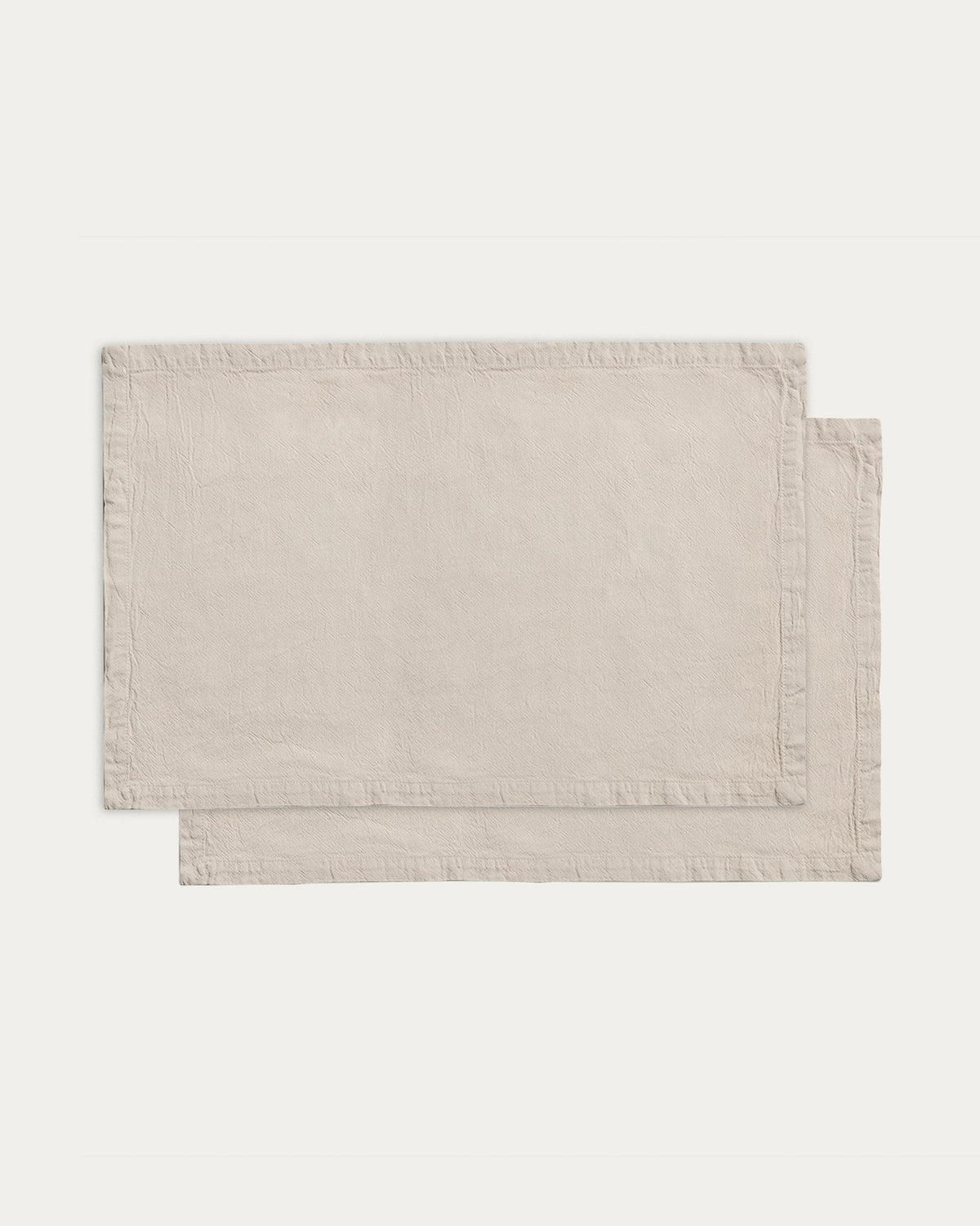 Zwei Tischsets aus Baumwolle mit steingrauem Washed-Finish und Leinen-Look, rechteckige Form, auf einem Tisch drapiert.