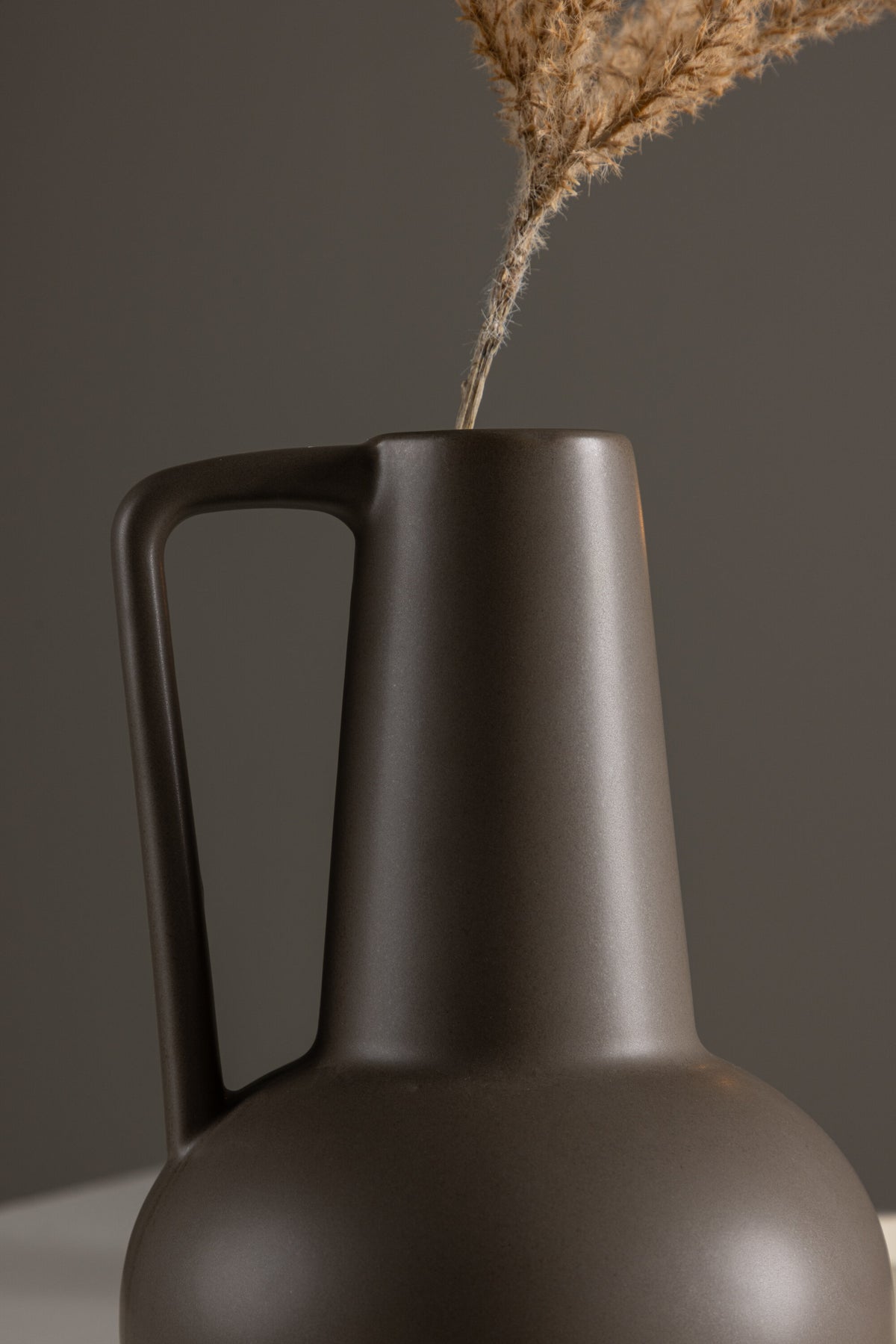 Zylindrische Vase aus Steinzeug in Beige und Schwarz mit seitlichem Griff, matte Oberfläche, Höhe 22 cm, Durchmesser 10 cm.