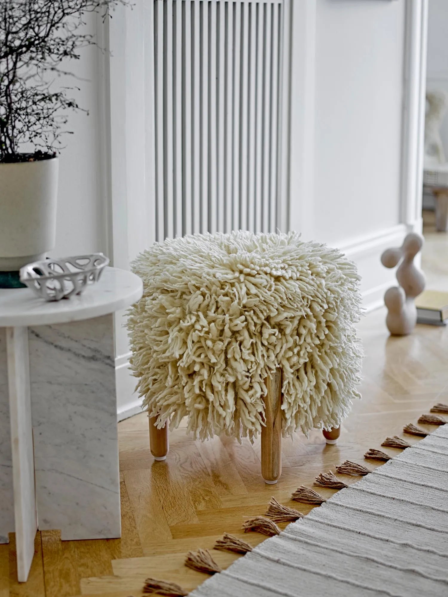 Eleganter Hocker aus natürlicher Wolle mit hellen Holzbeinen, ideal für stilvolle und gemütliche Wohnräume.
