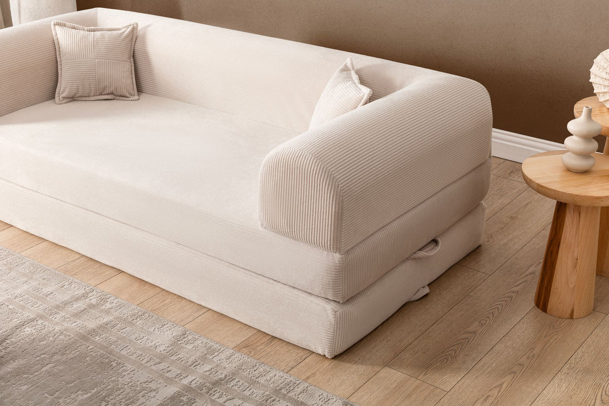 Cremefarbenes 3-Sitzer Schlafsofa Legom Eco von Hanah Home aus geripptem Cord-Plüschstoff mit zwei Kissen im Roll-Pack-Design abgebildet.