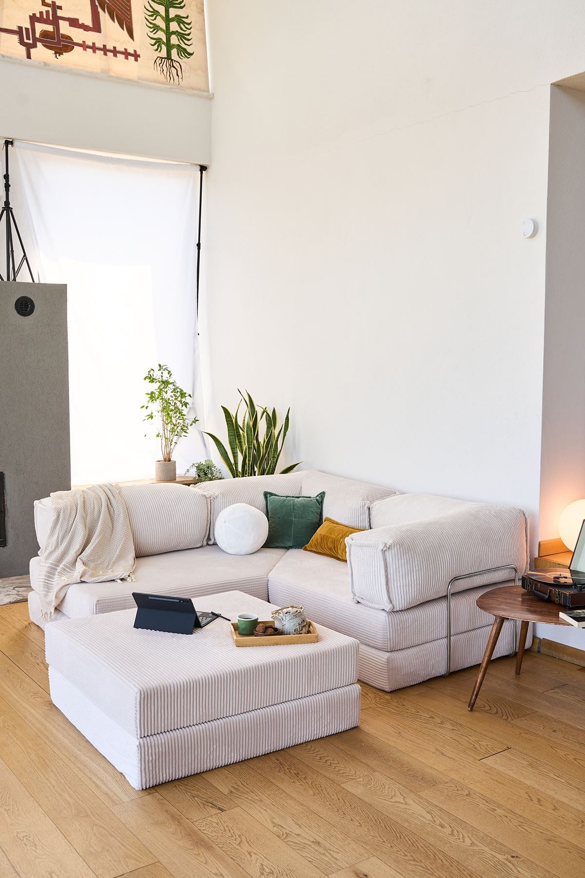 Cremefarbenes Eck-Schlafsofa aus Cord-Plüschstoff mit vier Kissen, rutschfester Sohle und abnehmbarem Bezug, Frontalansicht auf hellem Untergrund.