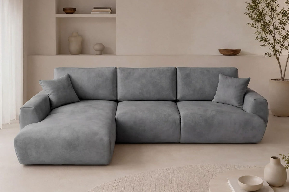 Graues Ecksofa Arthur mit Schlaffunktion, Gestell aus Buchenholz und Spanplatte, Bezug aus Polyester, Kunststoffbeine, zwei Kissen sichtbar.