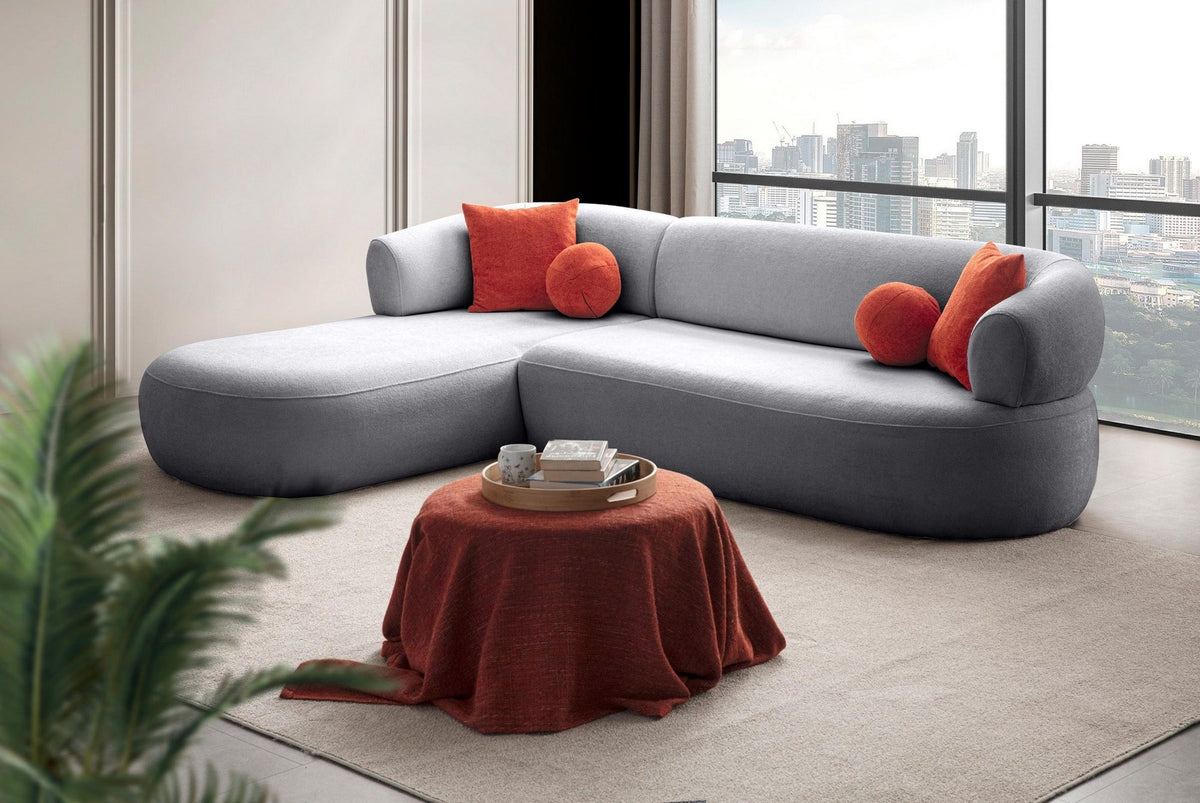 Graues Ecksofa links mit Boucle-Stoffbezug, Gestell aus Hainbuche und Spanplatte, Kunststoffbeinen und vier losen Kissen im Wohnzimmer.