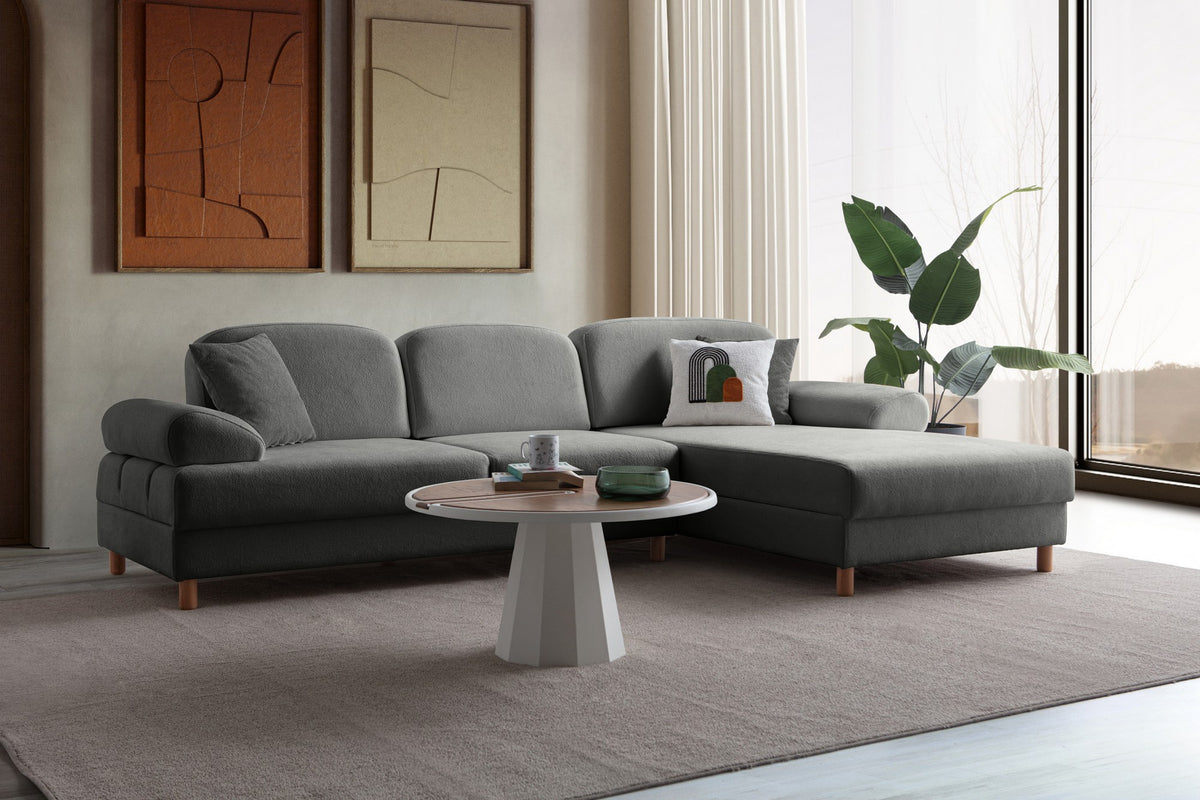 Anthrazitfarbenes Eck-Schlafsofa Aries von Hanah Home mit Coco-Boucle-Bezug, Holzbeinen und ausklappbarer Liegefläche in Wohnraumumgebung.