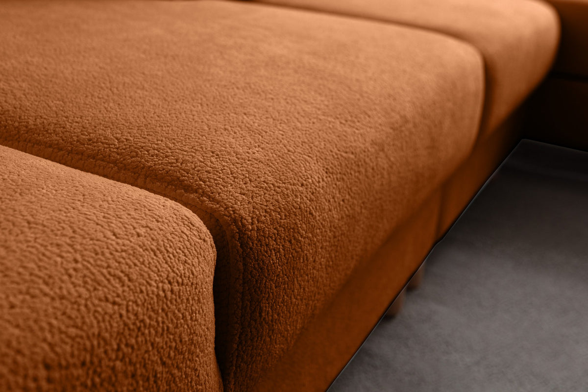 Eck-Schlafsofa Aries Relax Joker in Orange mit Coco-Boucle-Stoff, Holzbeinen und ausklappbarer Liegefläche, fotografiert im Wohnraum.