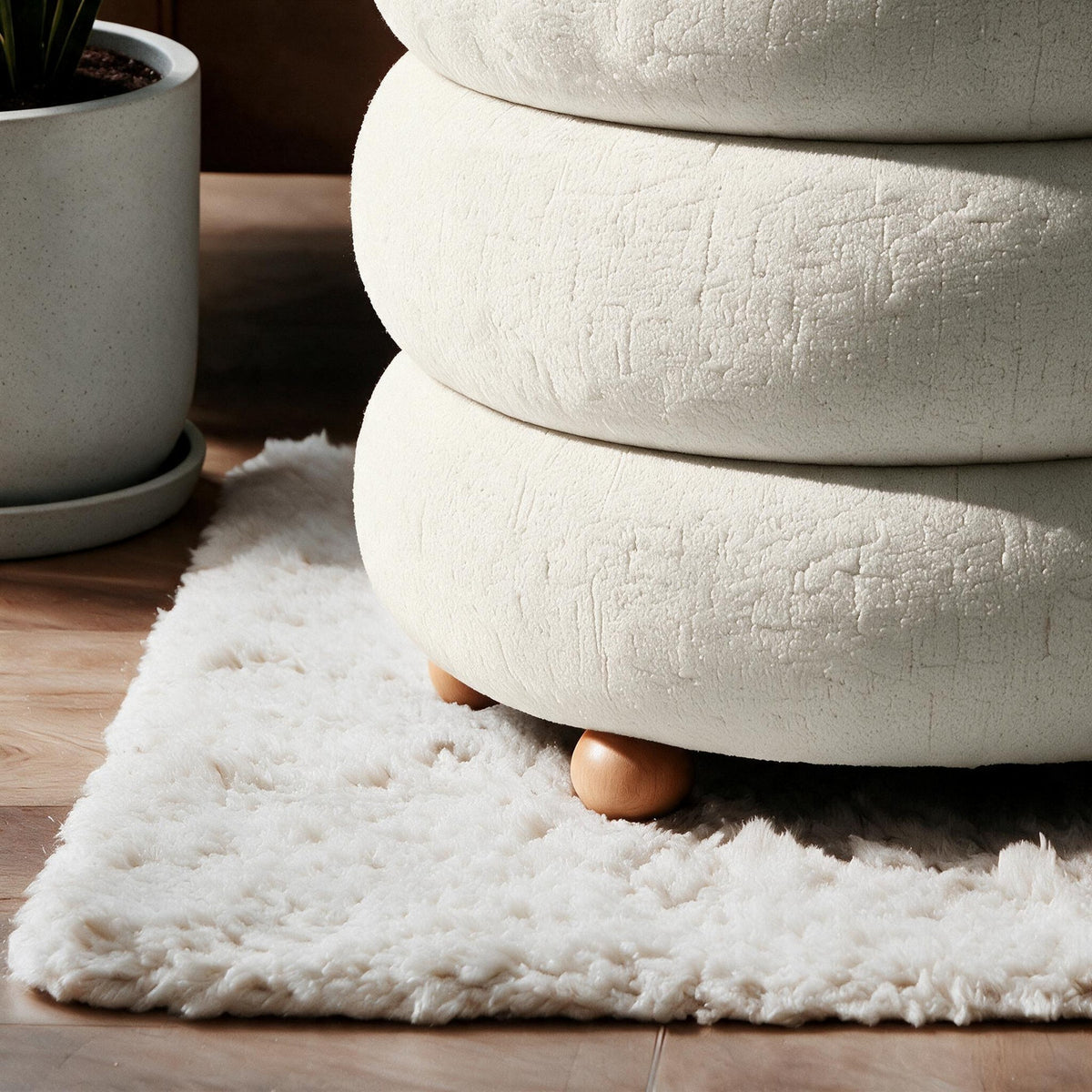 Runder Pouf in Off-White von Hanah Home mit gestricktem Polyesterbezug, Holz-Kugelfüssen und sichtbarem Stauraumfach im Innenraum.
