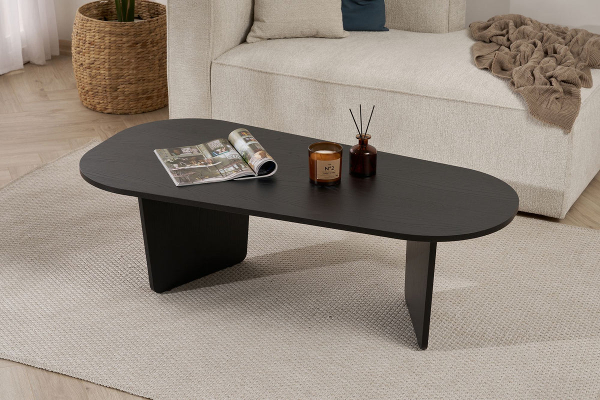 Ovaler Couchtisch aus melaminbeschichteter Spanplatte in Holz Schwarz, schlichte Form, Masse 130x65x40 cm, freistehend im Wohnraum.